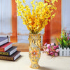 A gold-plated ceramic tabletop vase filled with bright yellow flowers on a light-colored table.