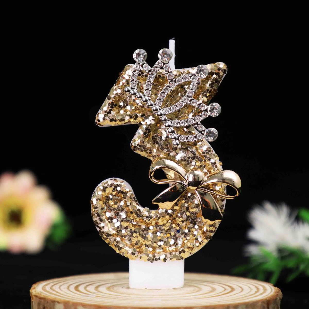 Gold glitter number cake topper featuring a rhinestone bow and candles on a wooden base.