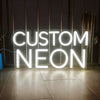 A glowing white neon sign spelling out CUSTOM NEON mounted on a dark wall.