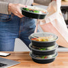 A person is holding a stack of round black meal prep containers with clear lids and food in them.