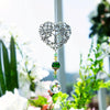 Silver crystal tree of life pendant with green and clear gemstone drops hanging in a garden setting