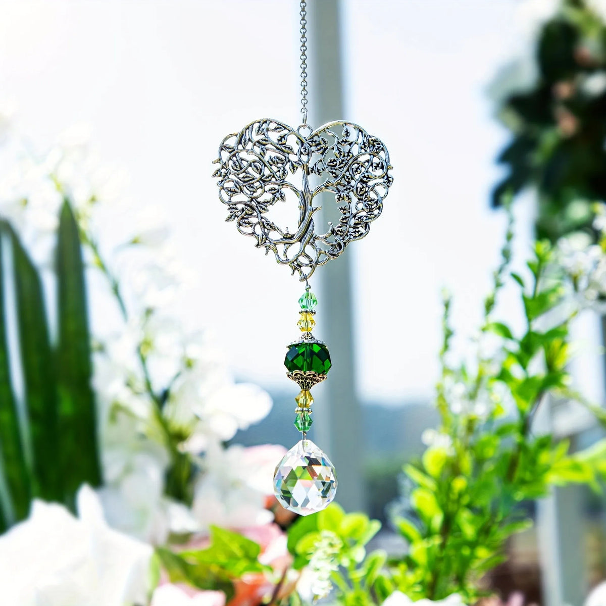 Silver crystal tree of life pendant with green and clear gemstone drops hanging in a garden setting