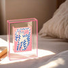 A pink acrylic photo frame holds a white and blue striped cat silhouette design.