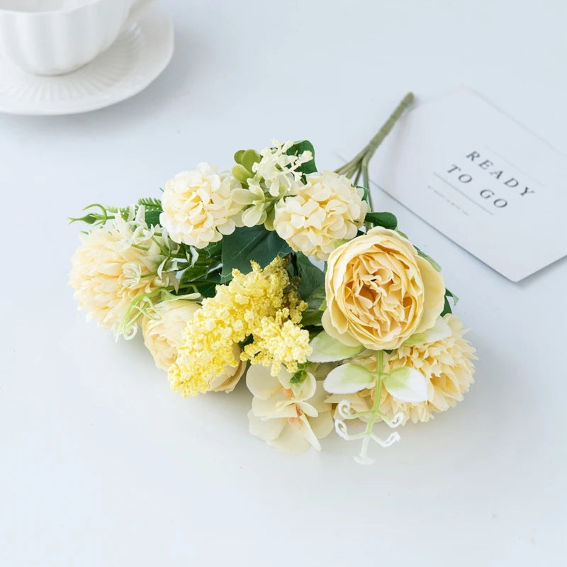 A bouquet of cream and yellow artificial silk peony flowers with green foliage placed next to a card that reads Ready to Go