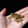 A brass money frog figurine resting on a human hand.