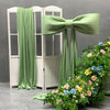 A light green satin bow with long tulle drape displayed next to a white door frame and floral greenery.