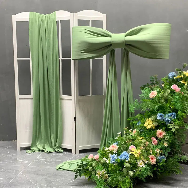 A light green satin bow with long tulle drape displayed next to a white door frame and floral greenery.