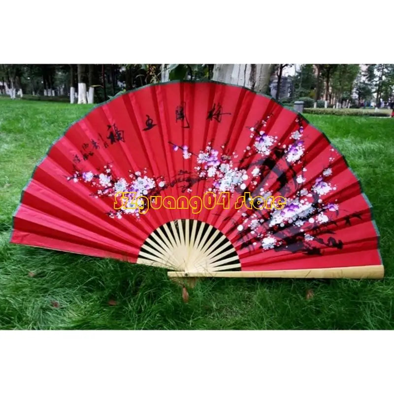 A large decorative red and pink fan with floral designs is displayed outdoors on green grass.