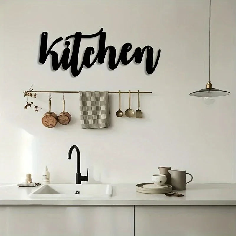 Black script wall art spelling kitchen above a kitchen rack with hanging utensils and a faucet