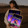 A person holds up a framed print featuring Minecraft characters and landscape art.