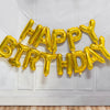 A string of gold foil letter balloons spelling out HAPPY BIRTHDAY decorating a white wall.