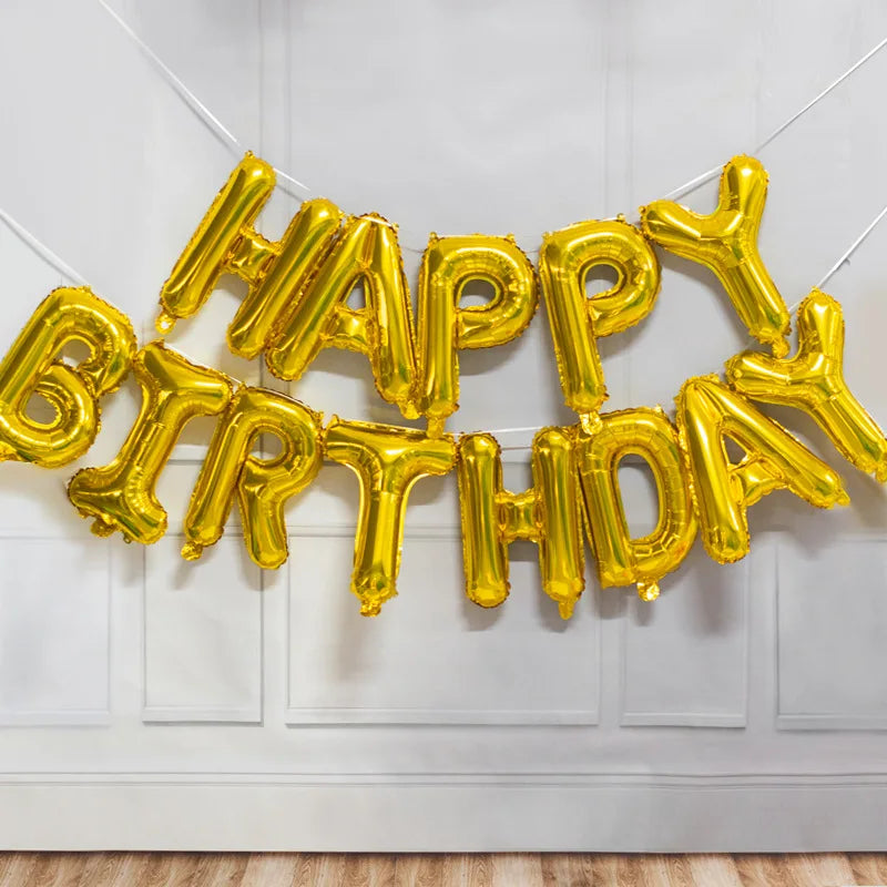 A string of gold foil letter balloons spelling out HAPPY BIRTHDAY decorating a white wall.