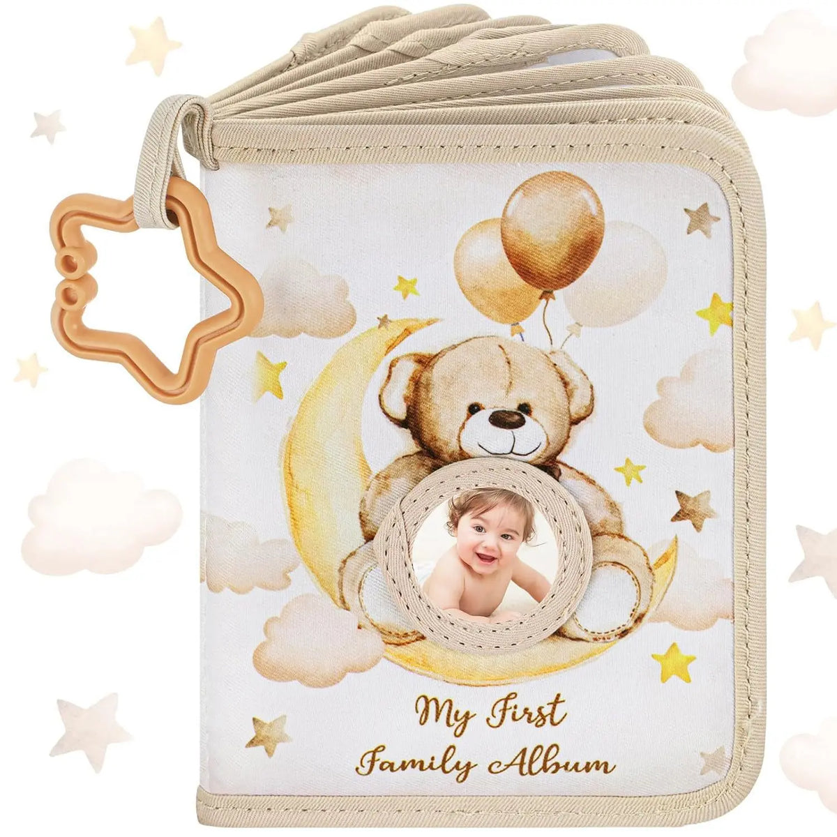 A beige fabric photo album cover featuring a teddy bear and a baby's face on a crescent moon against a cloud background.