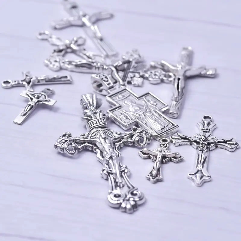 A collection of antique silver cross charms and pendants for jewelry making displayed on a white surface.