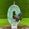 A white candle shaped like the number 4 decorated with green sequins and a purple butterfly on a wooden surface.