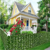 A bright yellow house with a porch and white railing is framed by a dense green artificial ivy hedge fence.