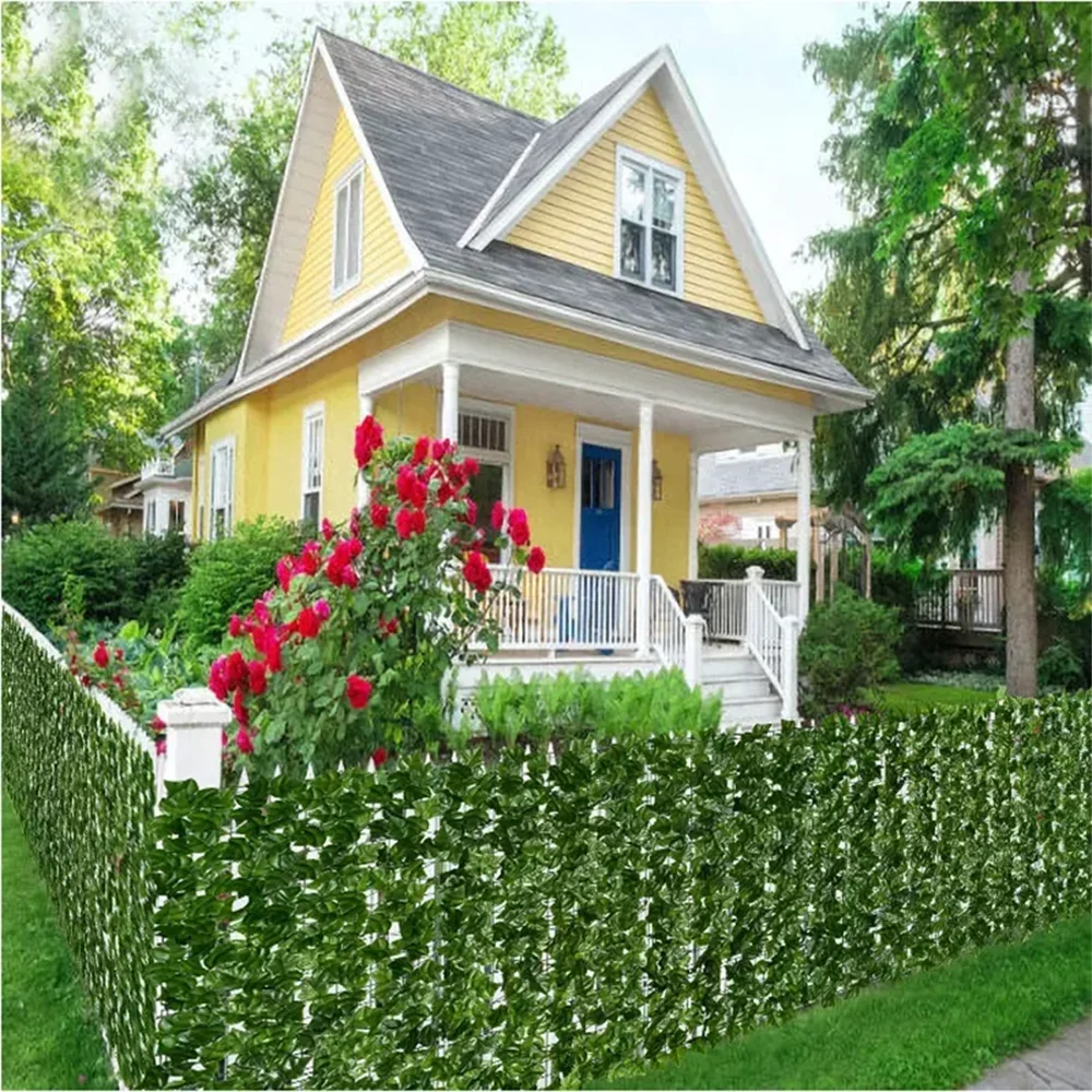 A bright yellow house with a porch and white railing is framed by a dense green artificial ivy hedge fence.