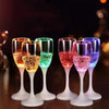 Une rangée de verres à boire LED multicolores clignotants remplis de liquides lumineux sur une surface sombre.