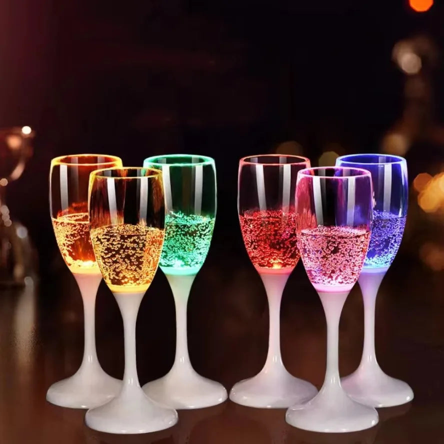 Une rangée de verres à boire LED multicolores clignotants remplis de liquides lumineux sur une surface sombre.