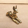 Handmade Egyptian Pharaoh dog statue in gold color resting on a light brown surface.