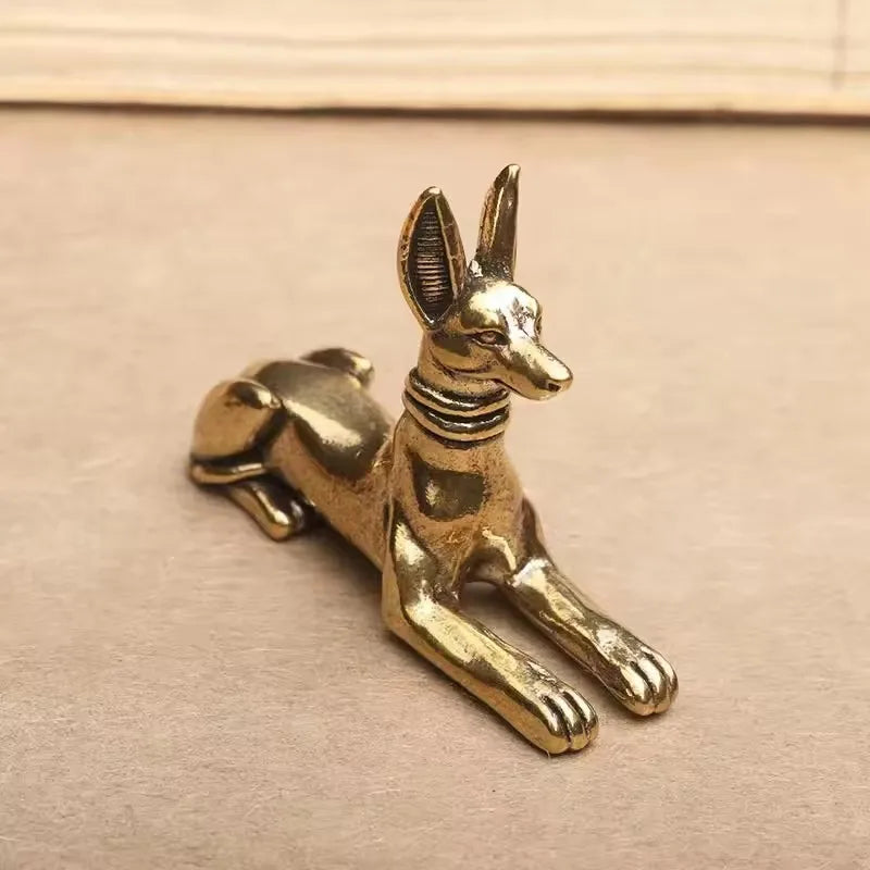 Handmade Egyptian Pharaoh dog statue in gold color resting on a light brown surface.