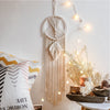 Boho macrame dream catcher wall decor featuring cream-colored macrame and fairy lights on a white wall.