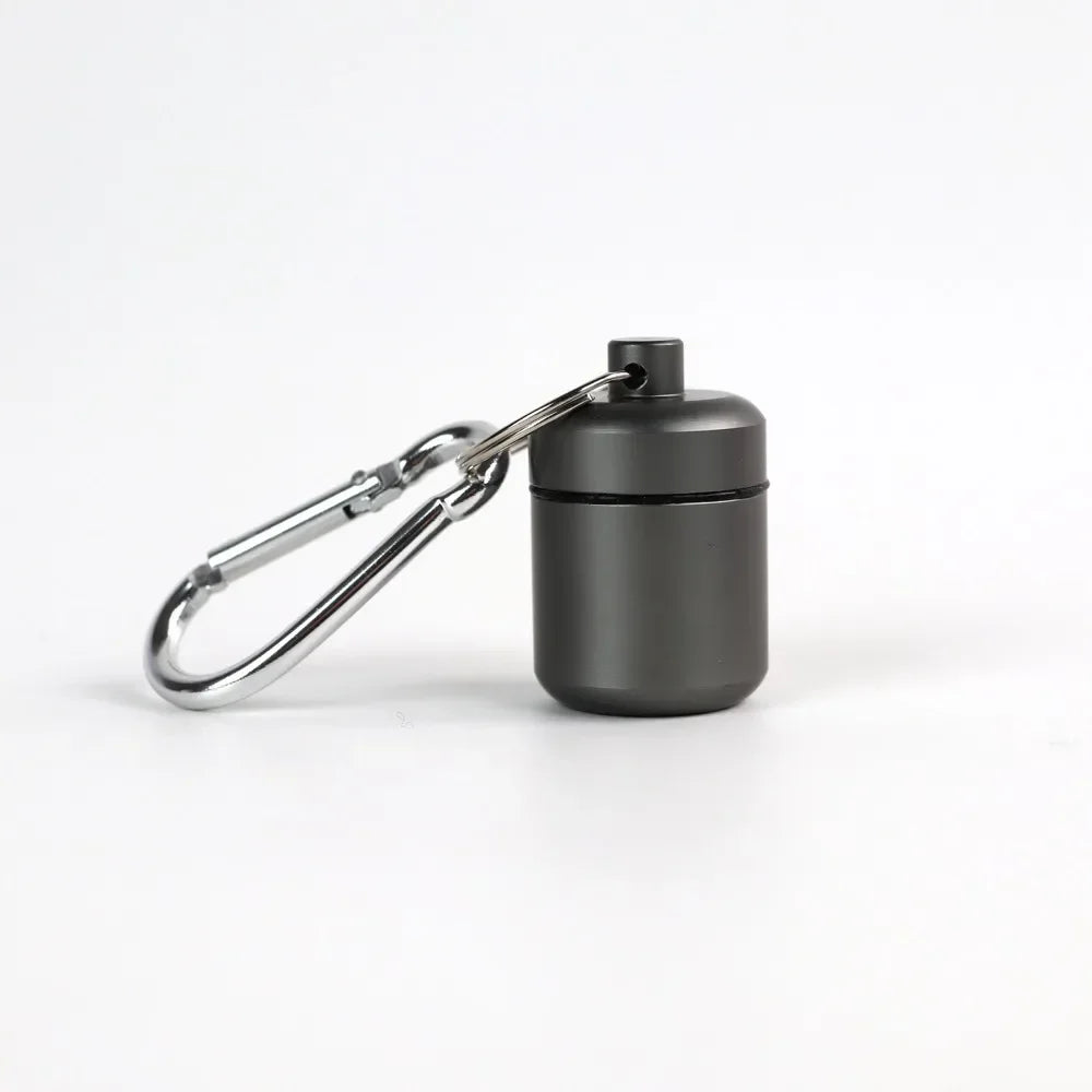 A small, black, cylindrical pill organizer is attached to a silver keychain ring.
