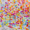 A pile of mixed colored faceted bicone glass beads in various shades including pink, orange, yellow, and blue.