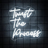 White neon sign on a dark surface displaying the text Trust The Process in a cloud shape.