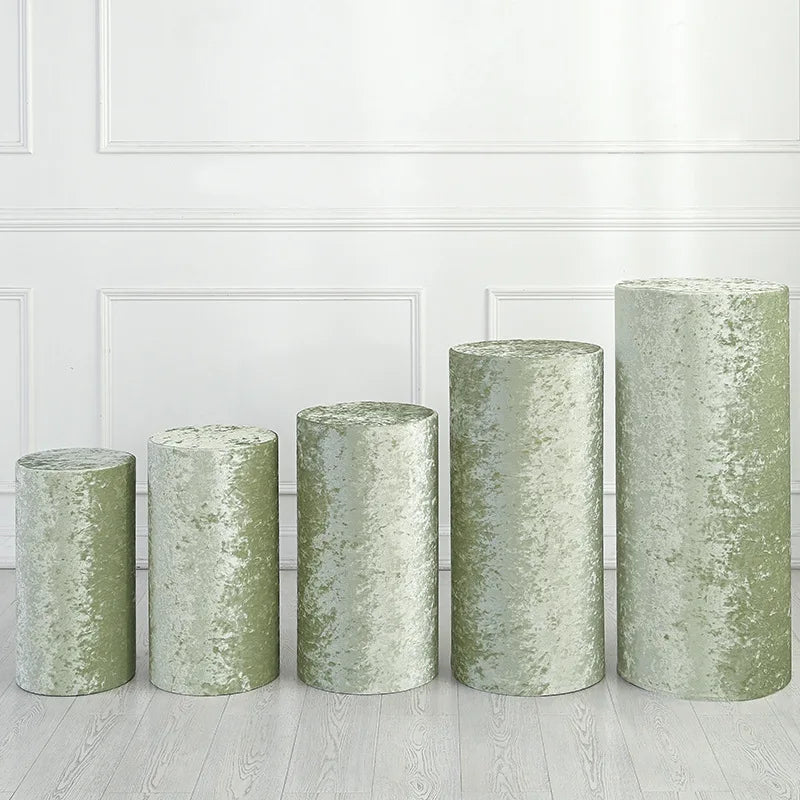 A row of four cylindrical green spandex stands used for wedding and event decor on a light wooden floor.