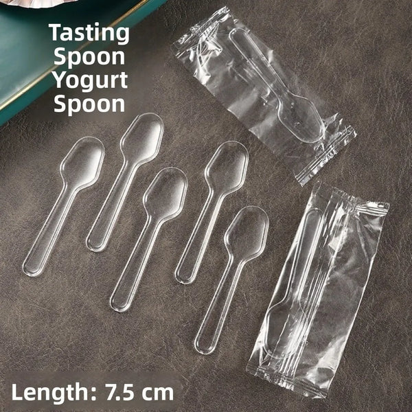 A collection of clear plastic disposable yogurt spoons laid on a dark surface.