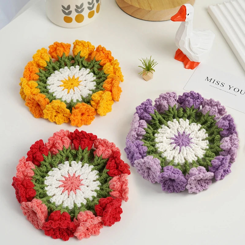 Three hand-crocheted rose flower coasters in orange, red, and purple displayed on a white surface.