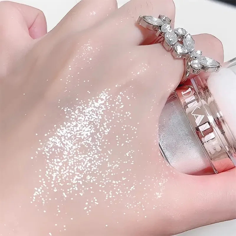 A hand is shown with a pink body glitter highlight powder applied to the skin and a silver ring.