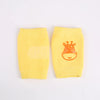 A pair of yellow knitted knee pads for crawling infants featuring an orange giraffe design.
