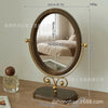 A round, gold-framed oval vanity mirror with a wooden base and a reflective surface.