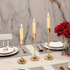 A set of three gold-toned minimalist retro tabletop candle holders with white taper candles on a marble surface.