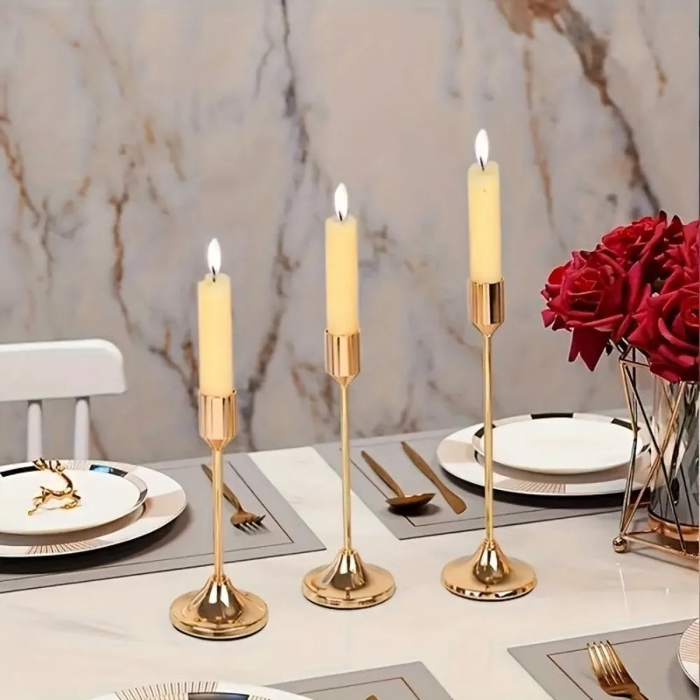 A set of three gold-toned minimalist retro tabletop candle holders with white taper candles on a marble surface.
