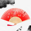 A vintage bamboo folding hand fan with red and white floral accents against a white background.