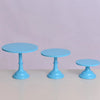 Three light blue metal cake stands with pedestal bases displayed on a light surface.