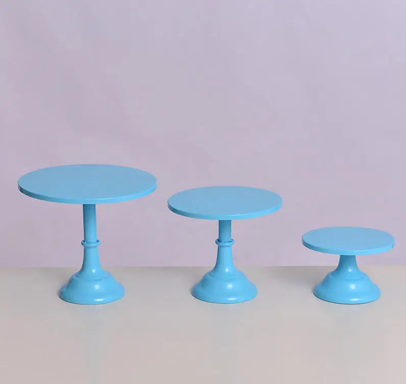 Three light blue metal cake stands with pedestal bases displayed on a light surface.