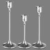 A set of three ornate vintage metal candle holders with slender stems and flared bases.