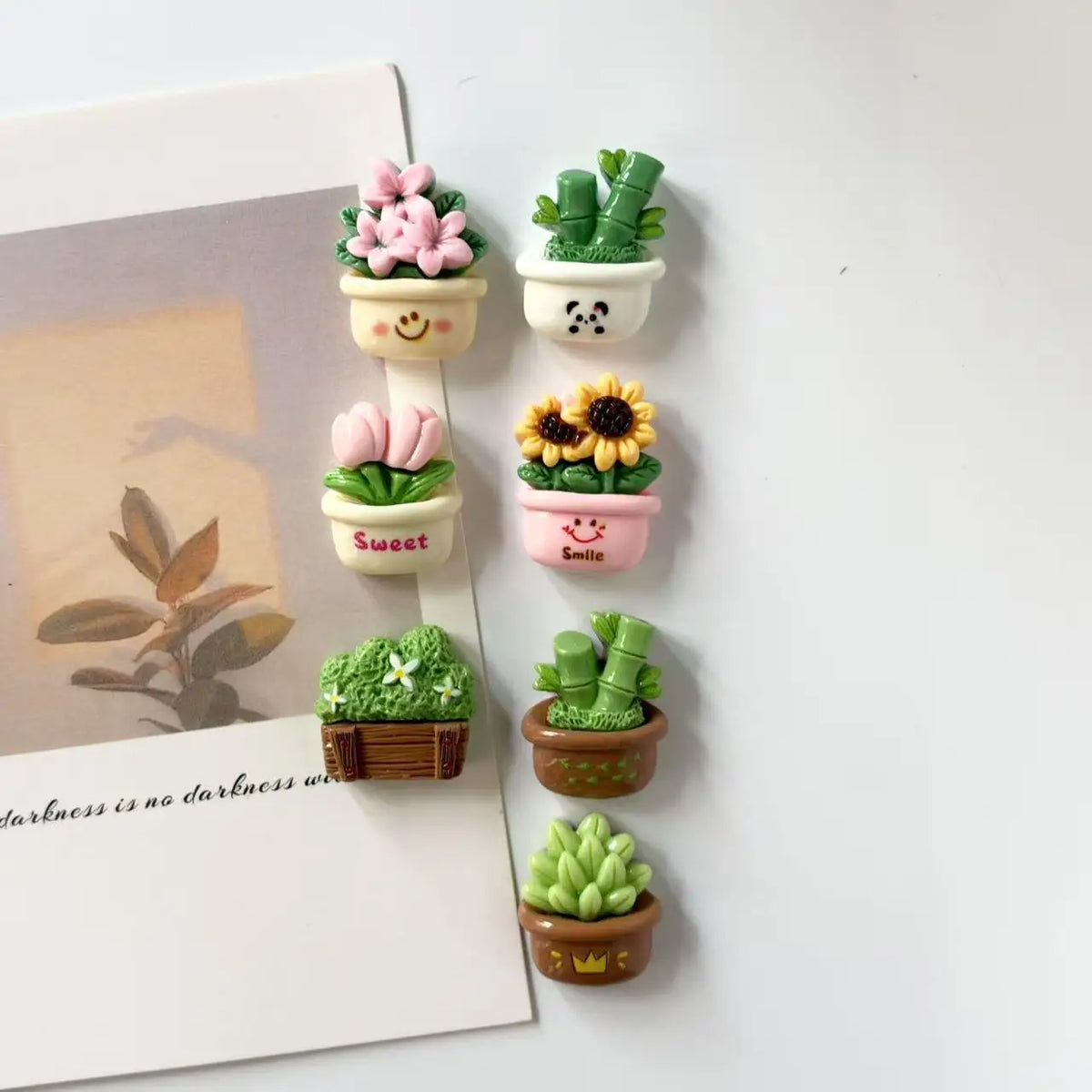 A set of seven small potted cactus plants in various colors and pots for desktop or kitchen decor.