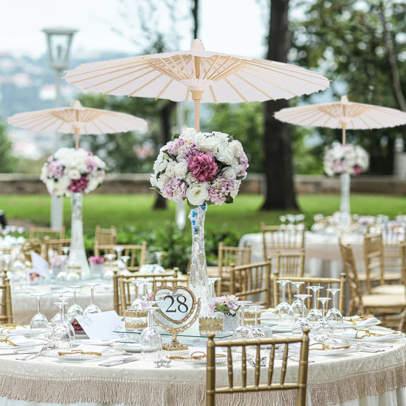 A table setting featuring gold chairs and white linens with a handcrafted white oil paper umbrella centerpiece.