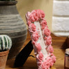 A pink rose resin picture frame is displayed on a wooden surface next to a potted plant and a gray vase.
