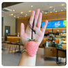 A hand holds a pink strawberry charm and keychain with a green leafy top against a blurred indoor background.