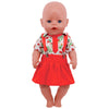 A baby doll wearing a red skirt and a shirt with a Christmas pattern.