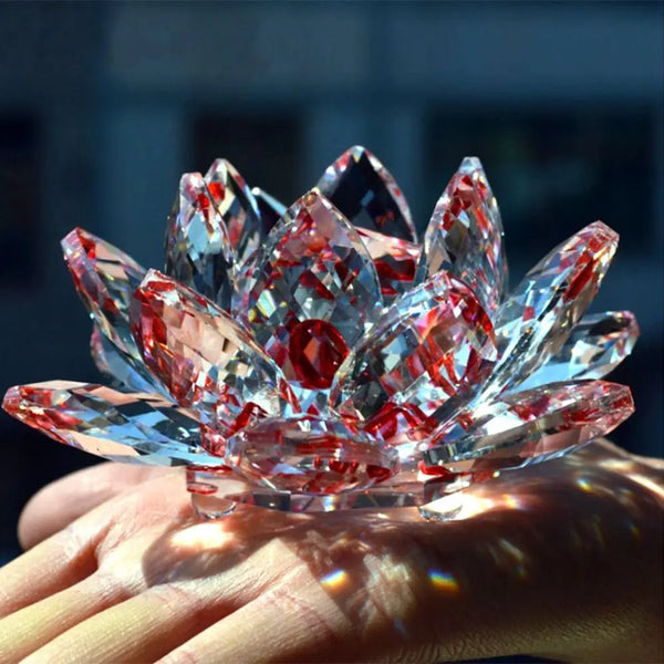 A hand holds a clear pink crystal lotus flower ornament sparkling with internal red hues.