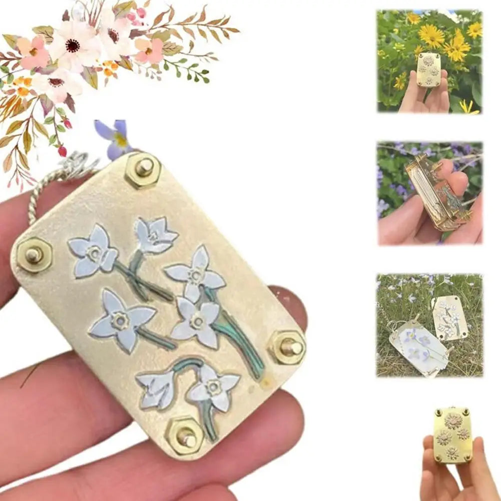A hand holds a pressed metal flower, surrounded by dried flowers and tools for crafting.