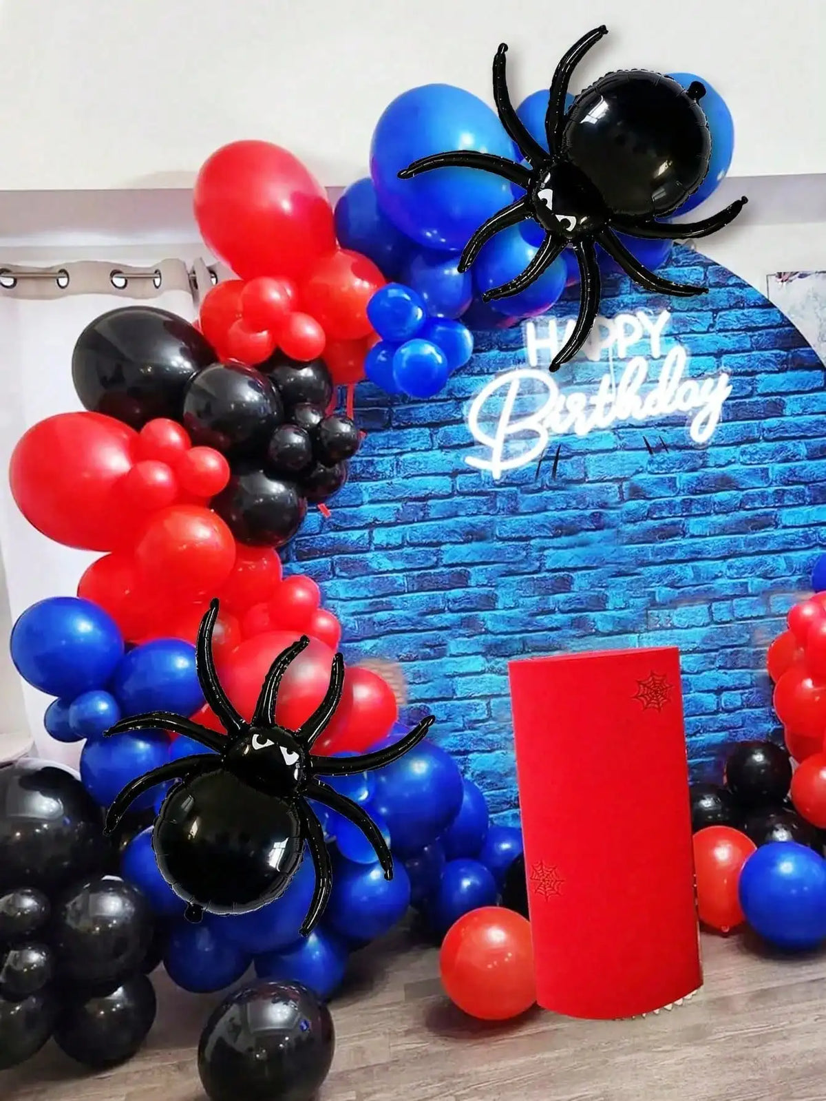Décoration d'anniversaire avec fond de briques bleues et ballons rouges, noirs et une araignée noire.