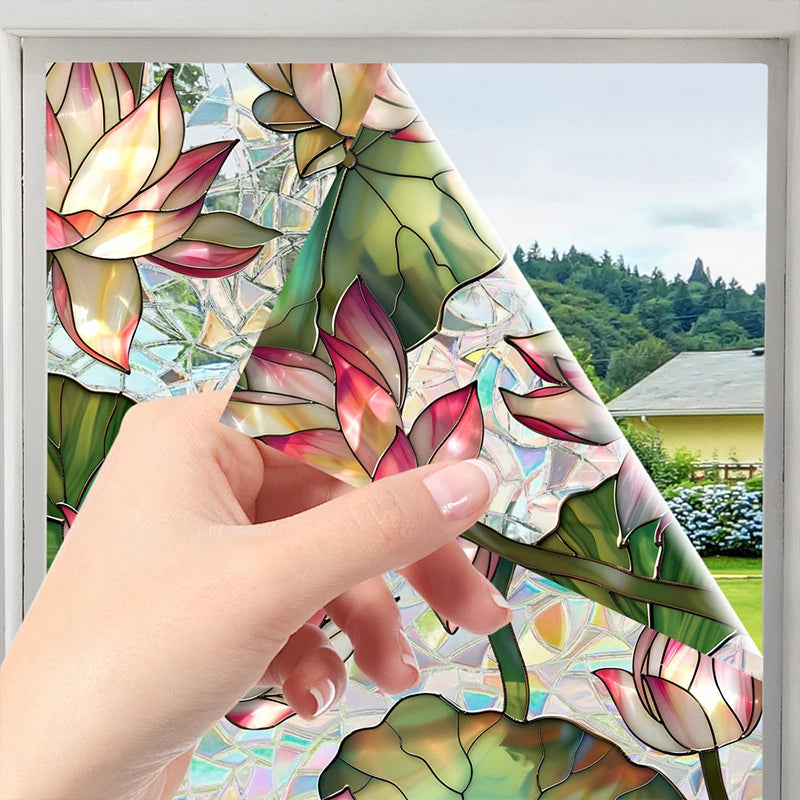 A hand is applying a botanical print static cling window film featuring pink and green floral designs onto a window pane.